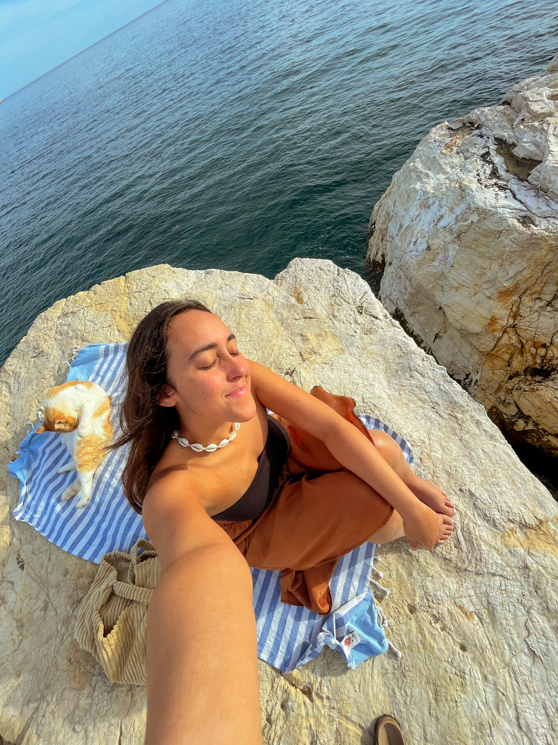 The Time Solo Traveling in Greece Made Me Jump Off A Cliff, girl sitting on a towel on a cliff