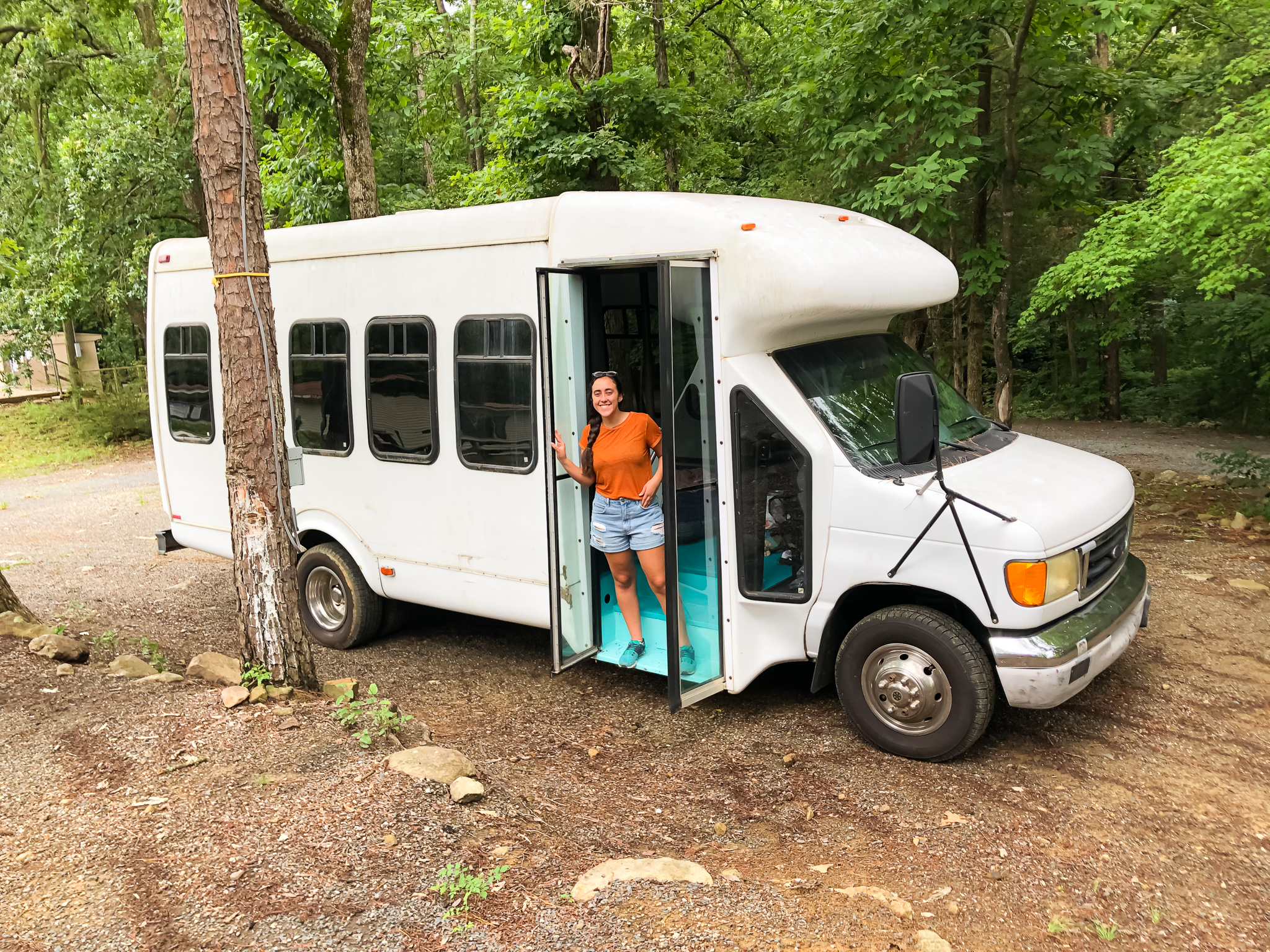 girl standing in the doorway of white shuttle bus in the woods