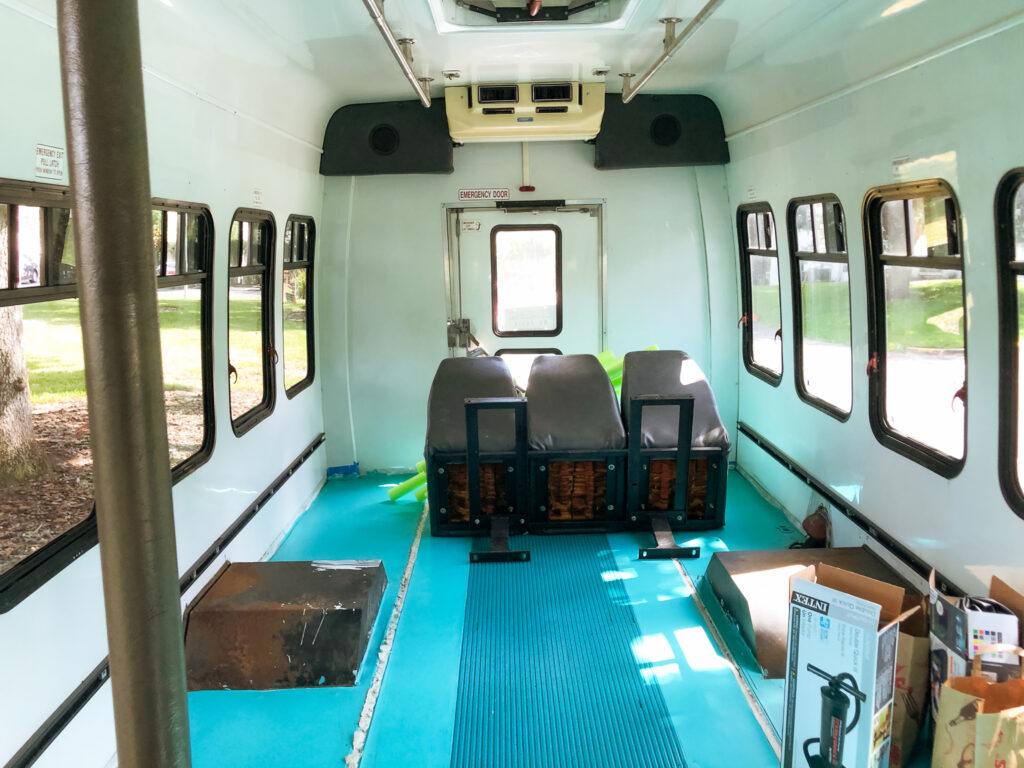 The inside of a shuttle bus with a teal floor and three loose seats.