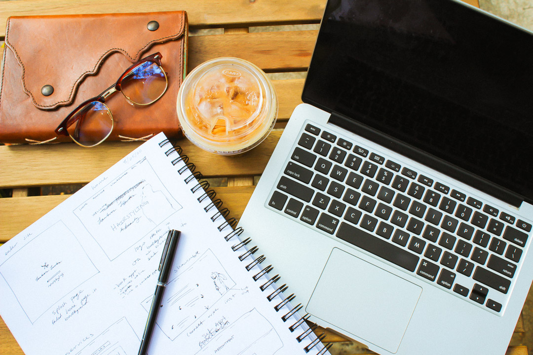 journal, glasses, coffee, computer and sketch book on a table